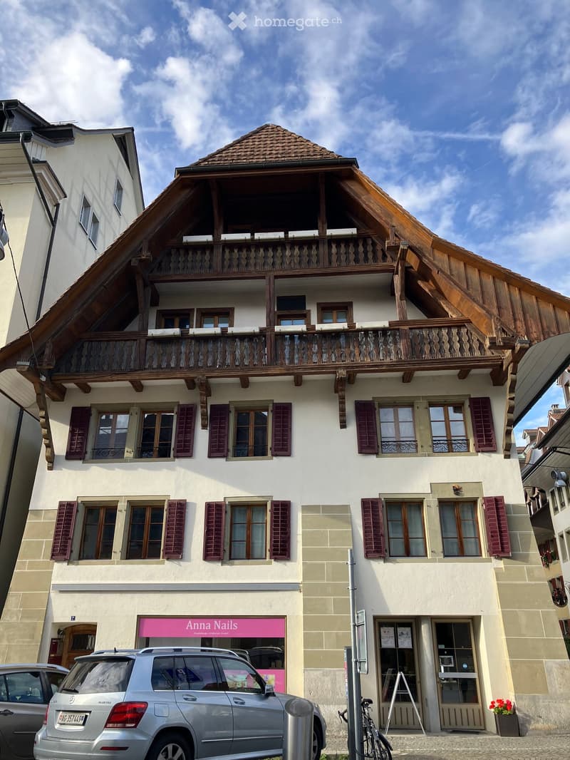 Three-story building with white facade, wooden balcony, multiple windows with shutters, and a storefront labeled 'Anna Nails'.