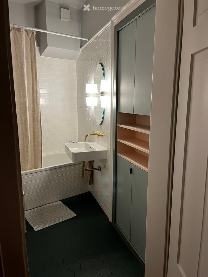 Modern bathroom with white subway tiles, hexagonal floor tiles, a white sink with gold faucet, a mirrored cabinet, and a bathtub with a shower curtain.