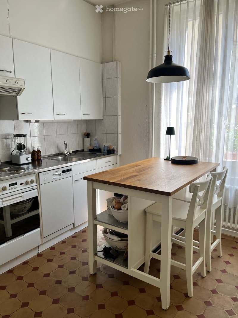 Modern kitchen with white cabinets, stainless steel appliances, a wooden island with two chairs, and a hanging pendant light.