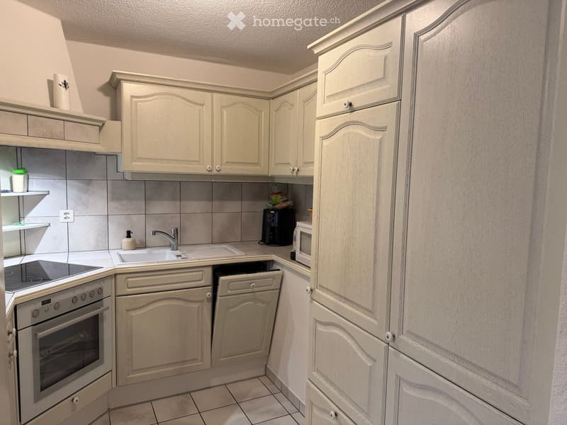 Modern kitchen with light-colored cabinets, a sink, oven, dishwasher, microwave, and toaster. The countertops are tiled, and the backsplash is gray.