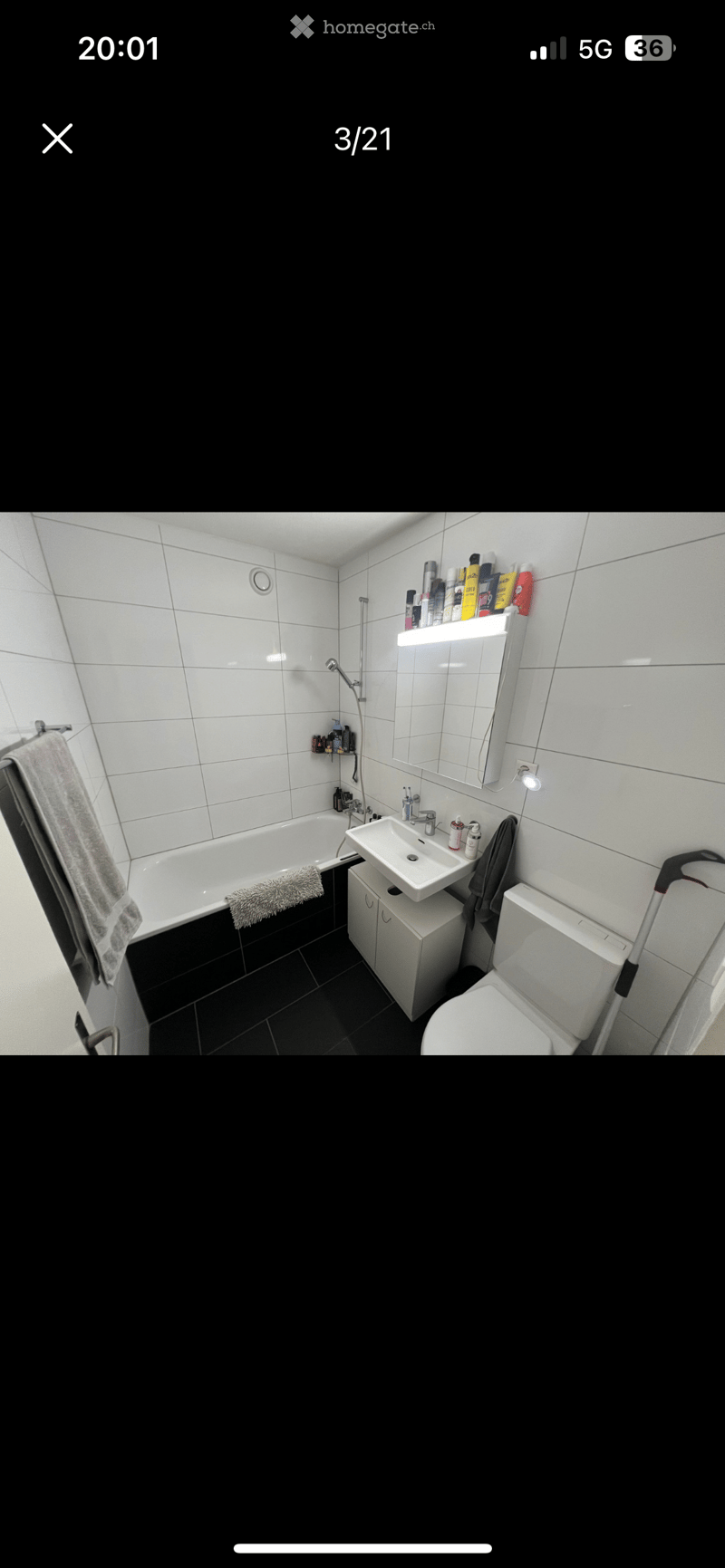 Modern bathroom with white tiled walls, black tiled floor, bathtub, sink, toilet, mirror, and towel.