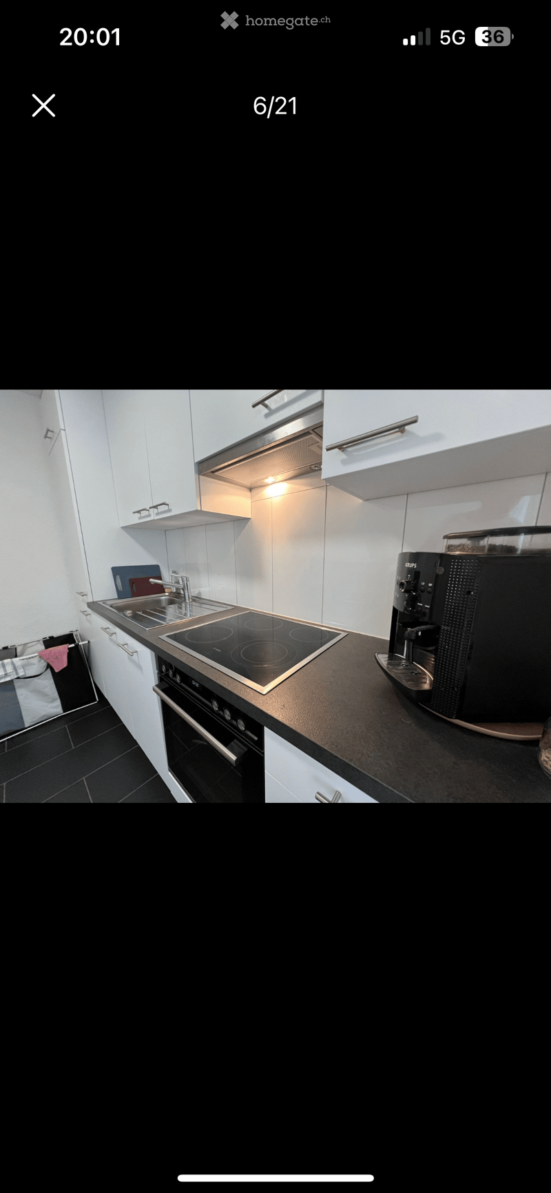 Modern kitchen with white cabinets, black countertops, induction cooktop, oven, coffee machine, and a sink with a faucet.