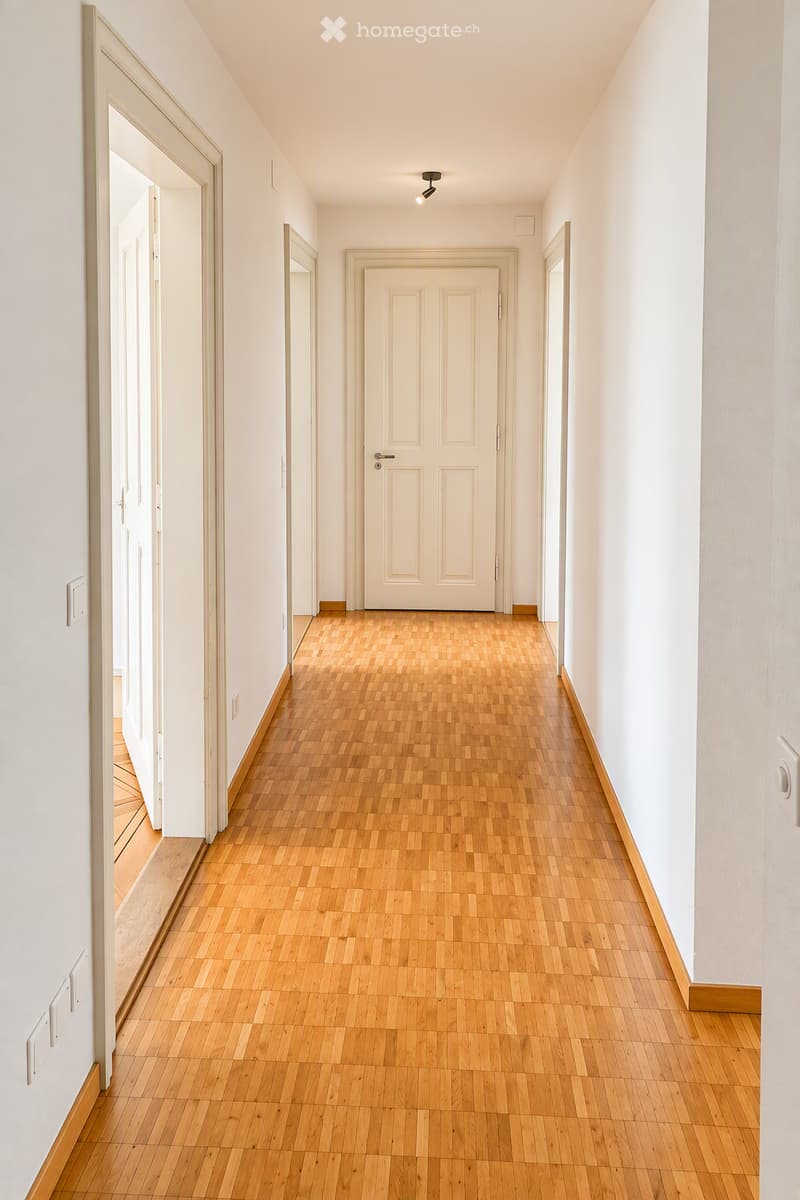 Empty hallway with light wooden flooring, white walls, and several doors leading to other rooms.