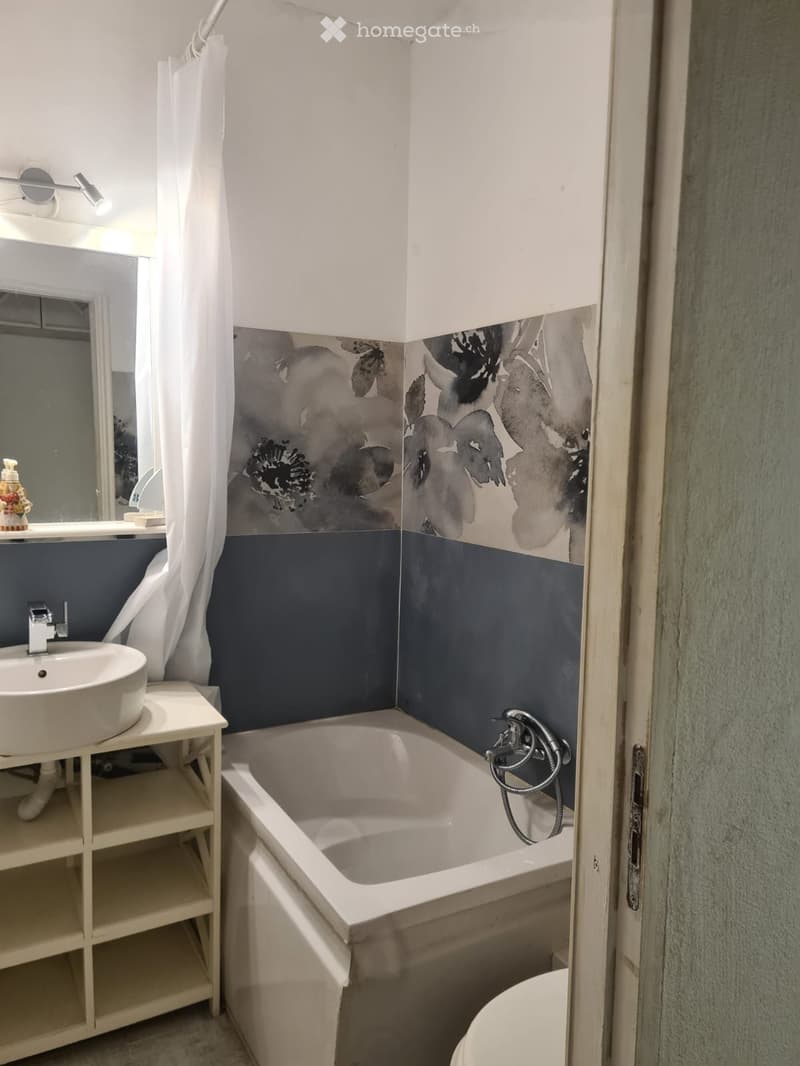Bathroom with a white bathtub, a white sink on a small shelf, a mirror, and a shower curtain with a floral design. The walls are painted in two tones: dark blue at the bottom and white at the top.