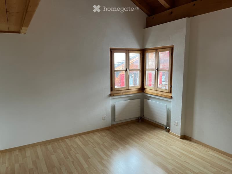 Empty room with wooden flooring, white walls, and large windows with wooden frames. Radiators are present under the windows.