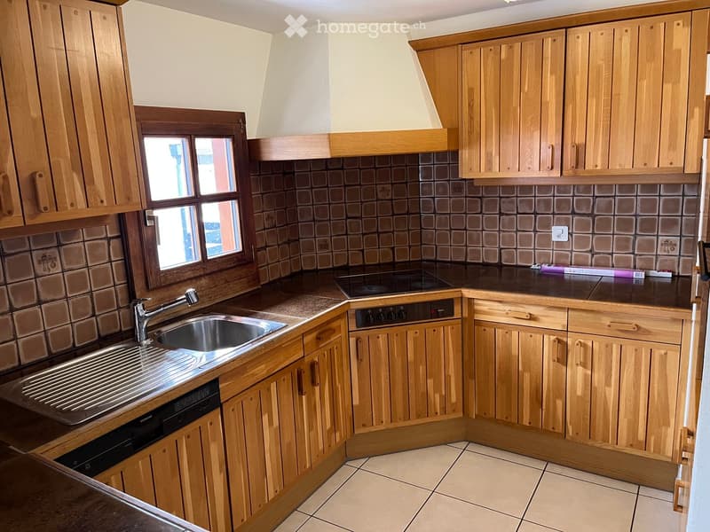 Well-lit kitchen with wooden cabinets, a stainless steel sink, a dishwasher, and a stove. The backsplash features dark brown tiles, and the countertops are black.