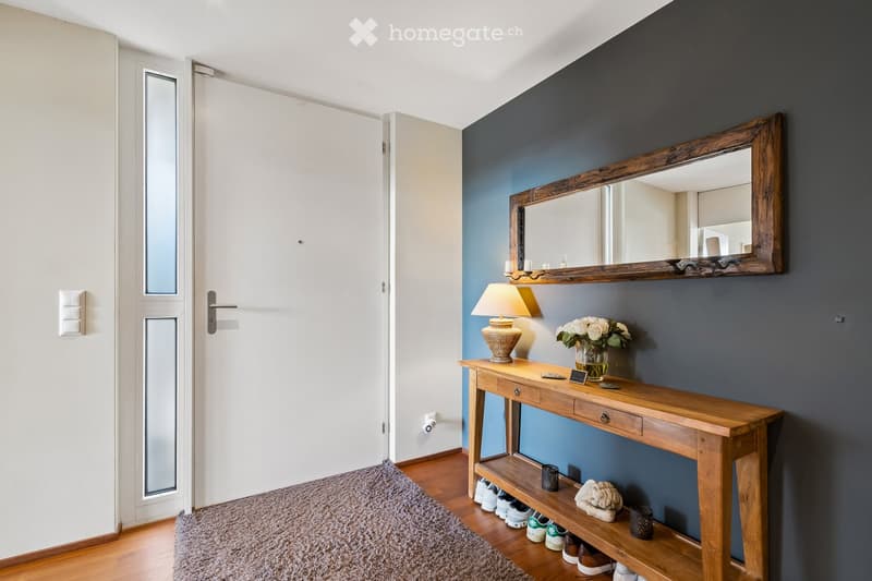 A modern hallway with a wooden console table, a lamp, a mirror, a vase with flowers, and a shoe rack below.