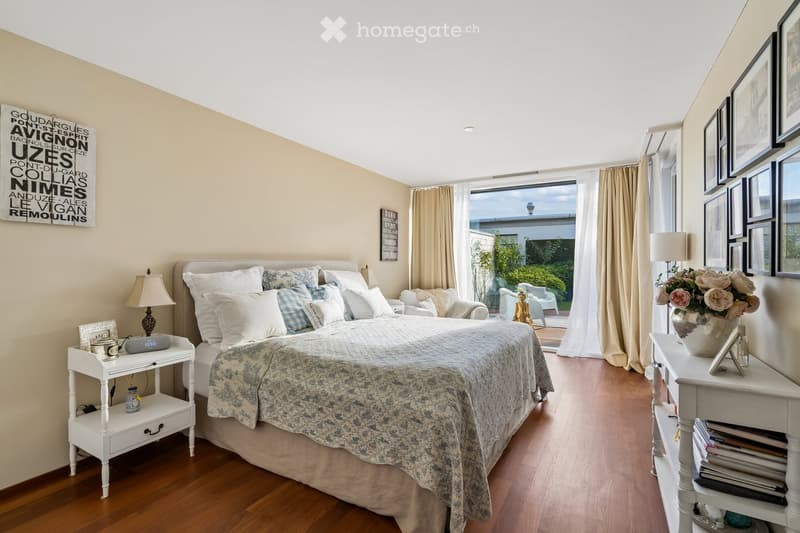 Elegant bedroom with a large bed, nightstands, lamps, and a view of a garden through large windows.