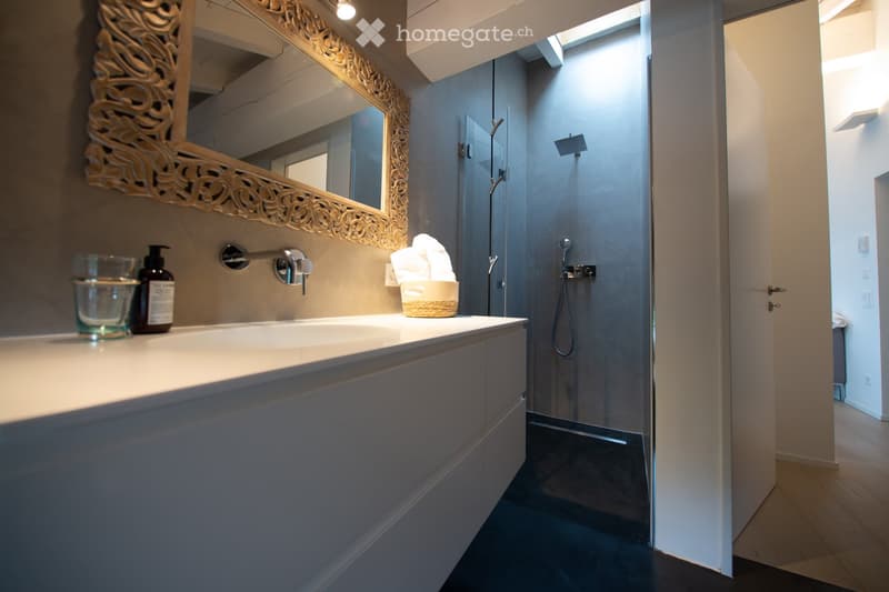 Modern bathroom with a white sink, decorative mirror, glass shower enclosure, and neatly placed towels.