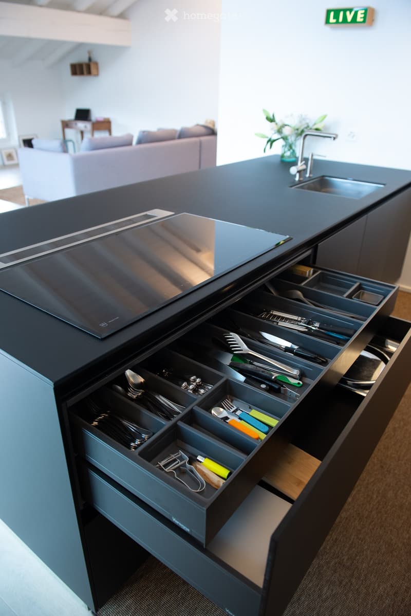 Modern kitchen with black countertops, open drawers filled with cutlery and utensils, and a sleek sink with a modern faucet.