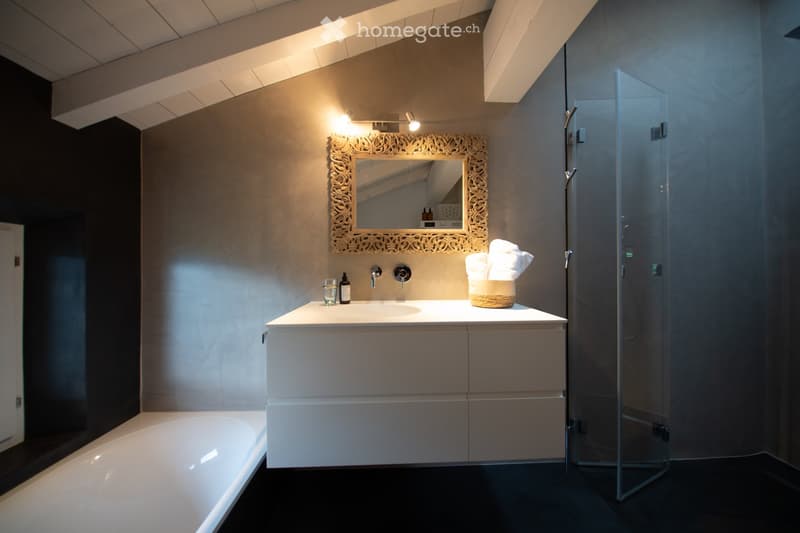 Modern bathroom with a white bathtub, a white sink with a vanity cabinet, a decorative mirror, a glass-enclosed shower, and a towel on a woven basket.