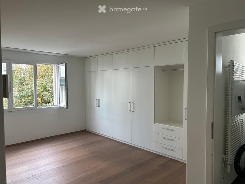 Empty room with light-colored wooden flooring, white built-in wardrobes, and large windows letting in natural light.