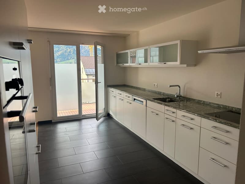Modern kitchen with white cabinets, granite countertop, sink, and dishwasher. Large sliding glass door opens to a balcony.