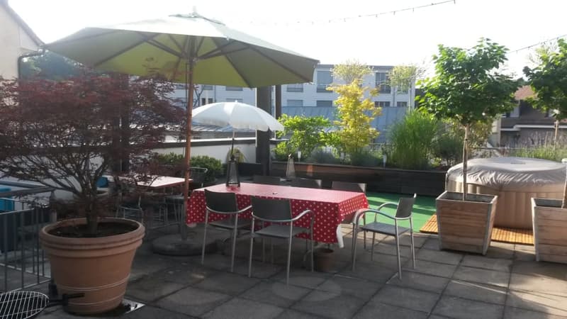 Outdoor patio with a dining table, chairs, umbrellas, potted plants, and a hot tub.
