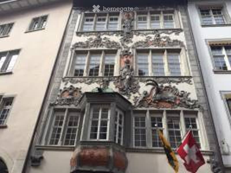 Ornate historic building facade with intricate carvings, multiple windows, and flags displayed on the side.