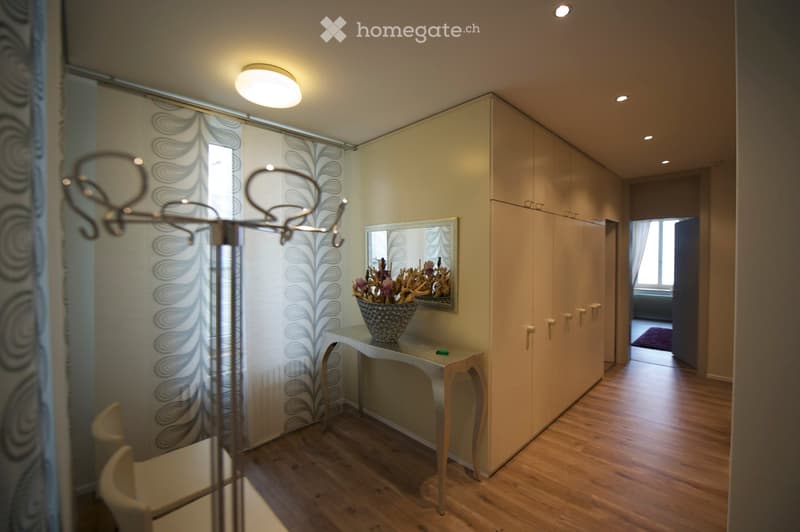 Elegant hallway with wooden flooring, a small table with a decorative vase, a large mirror, and built-in wardrobes.