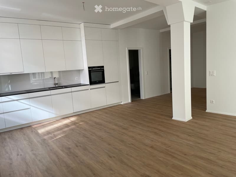 Modern kitchen with white cabinets, a sink, and an oven, featuring wooden flooring and ample natural light.