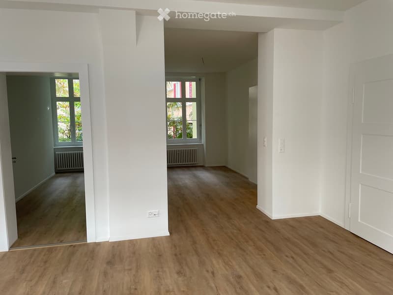 Empty room with wooden flooring, white walls, and large windows. No furniture or equipment present.