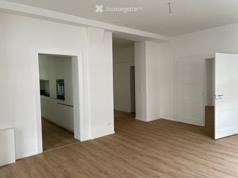 Empty room with wooden flooring, white walls, and multiple doors leading to other rooms.