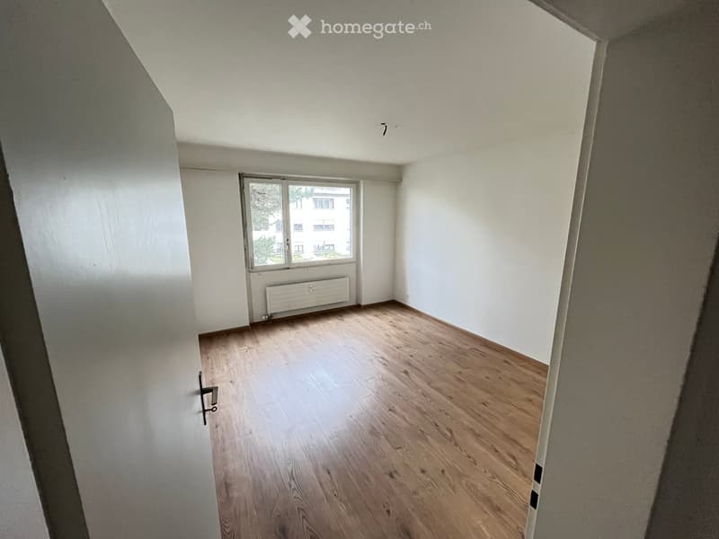 Empty room with wooden flooring, white walls, and a window with a radiator below it.