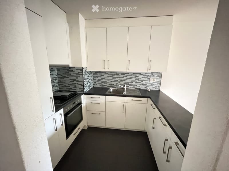 Modern kitchen with white cabinets, black countertops, and a stainless steel sink. Features an oven and sleek design.