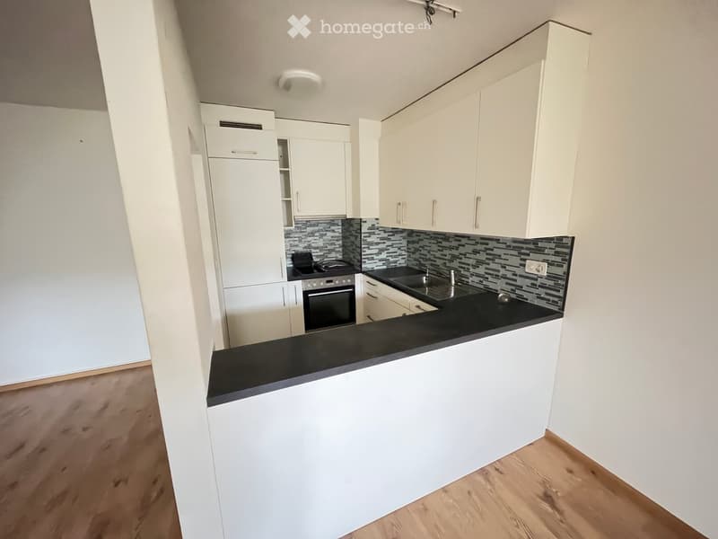 Modern kitchen with white cabinets, black countertop, stainless steel sink, and oven. Features a sleek design with a mosaic tile backsplash.