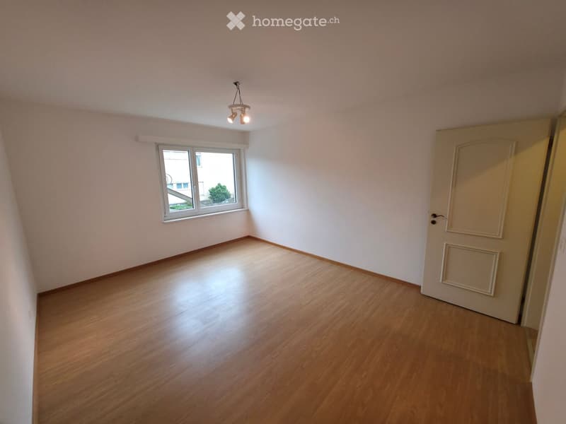 Empty room with wooden flooring, white walls, a single window, and a closed door.