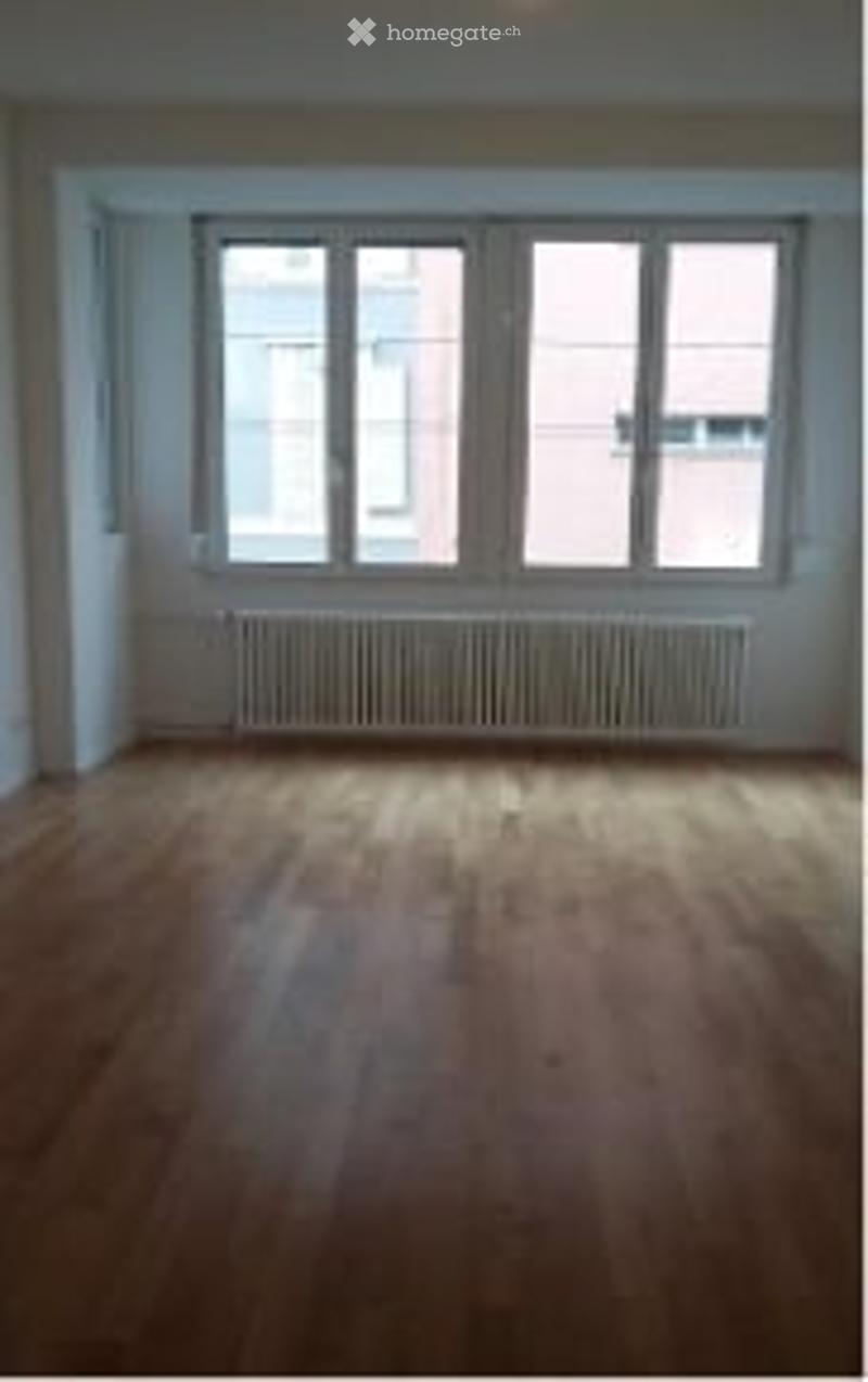 Empty room with wooden flooring, large windows, and a radiator below the windows.