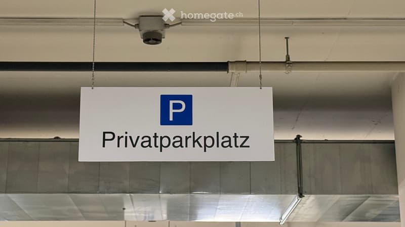 A sign reading "Privatparkplatz" (private parking space) is suspended from the ceiling in a building corridor.