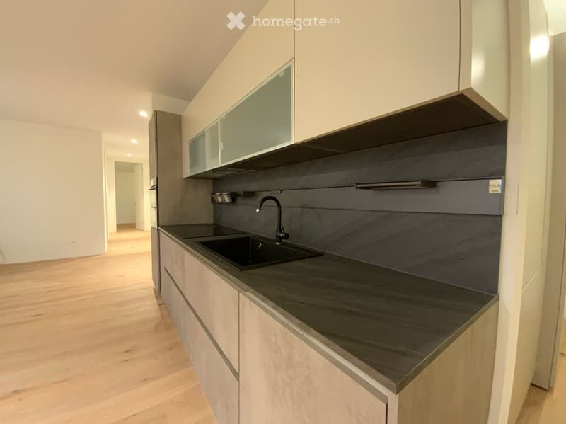 Modern kitchen with light wooden cabinets, dark countertop, and a black sink with a chrome faucet.
