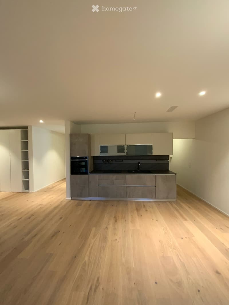 Empty kitchen with light wooden flooring, modern cabinetry, and built-in appliances including an oven and sink.