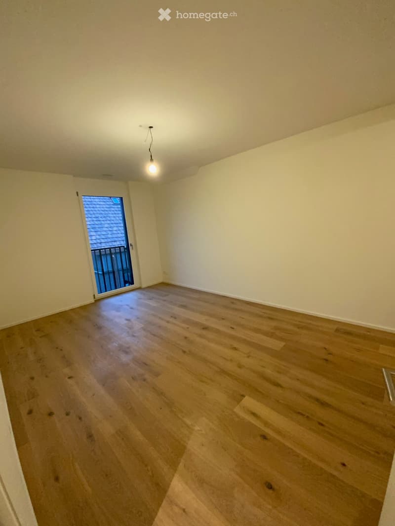 Empty room with wooden flooring, white walls, and a sliding door leading to a balcony.