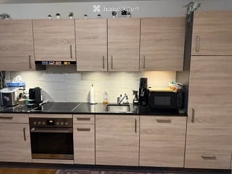 Modern kitchen with light wood cabinets, stainless steel appliances, and built-in lighting.