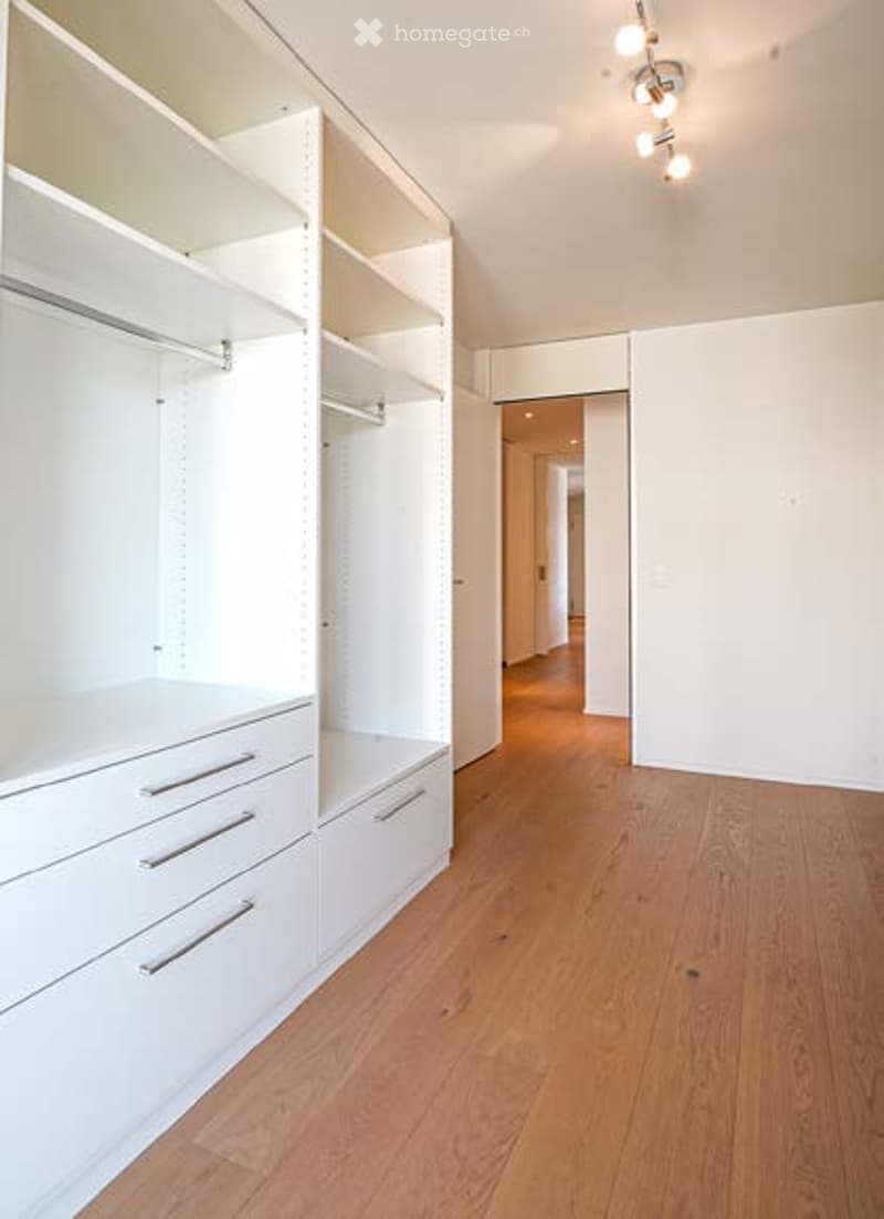 Empty room with white built-in closet and drawers, wooden flooring, and recessed lighting.