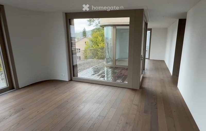 Empty hallway with wooden flooring, large glass doors leading to a balcony area with outdoor view.