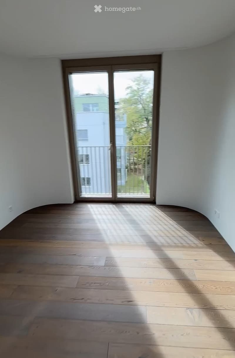 Empty room with wooden flooring and white walls, featuring a large sliding glass door leading to a balcony.