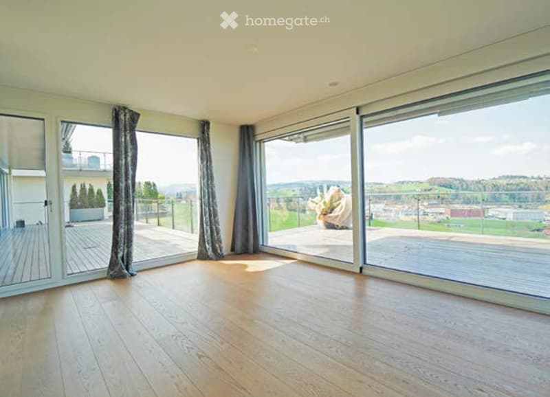 Bright, empty room with large floor-to-ceiling windows and sliding glass doors leading to a balcony with scenic views.