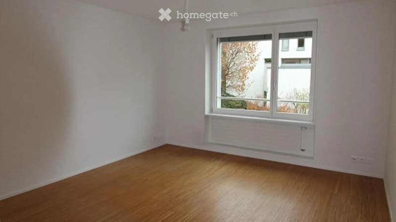 Empty room with wooden flooring and white walls, featuring a large window with white frame and a radiator below it.