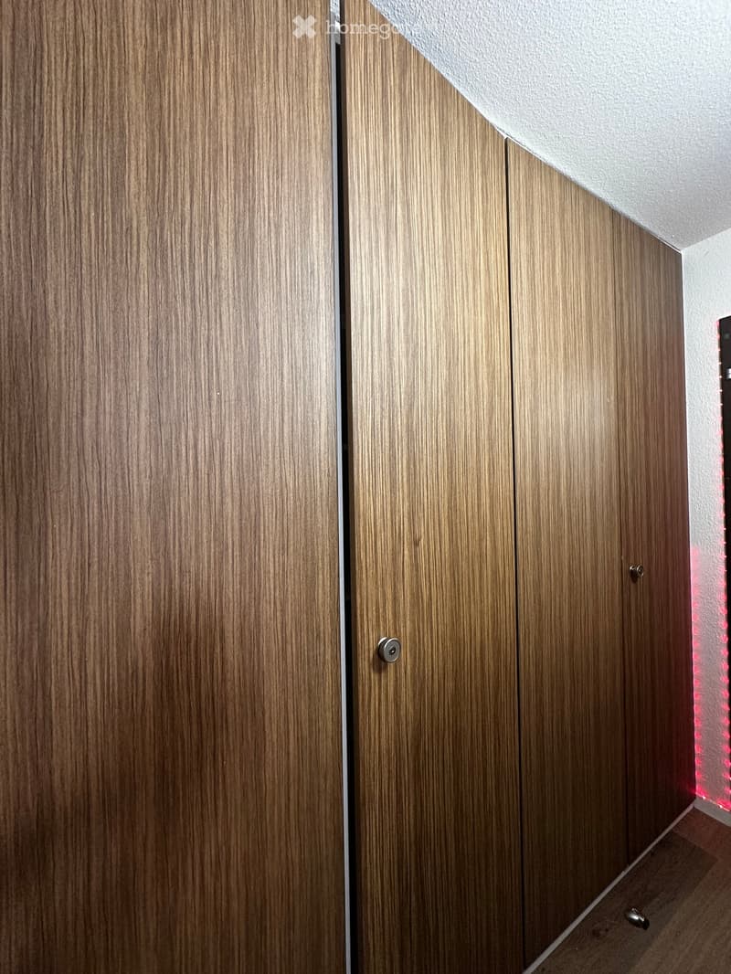A narrow hallway with wooden paneled walls and a light-colored ceiling. The hallway features two closed wooden doors with silver handles and a small section of red lighting visible on the right side.