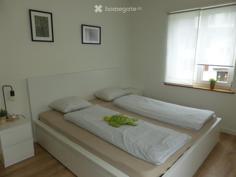 Cozy bedroom with two single beds, nightstand, lamp, and decorative picture frames on the wall.