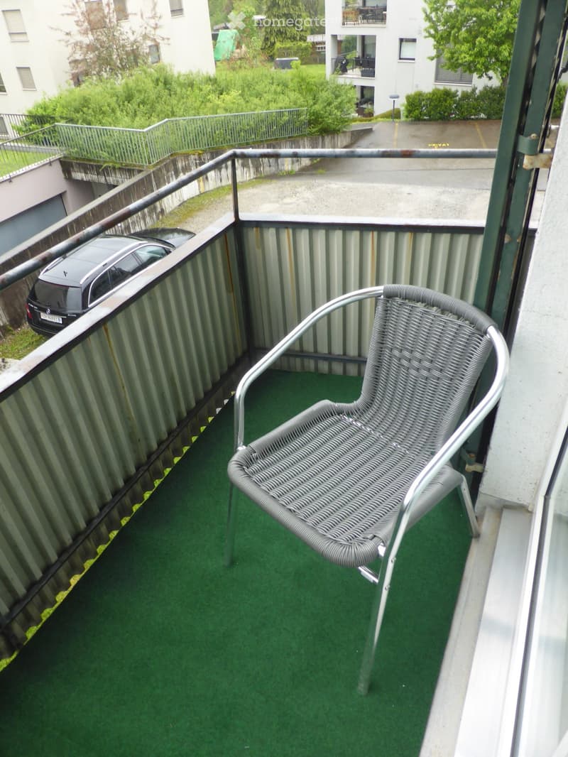 Balcony with green artificial turf flooring, metal railing, and a single metal wicker chair.
