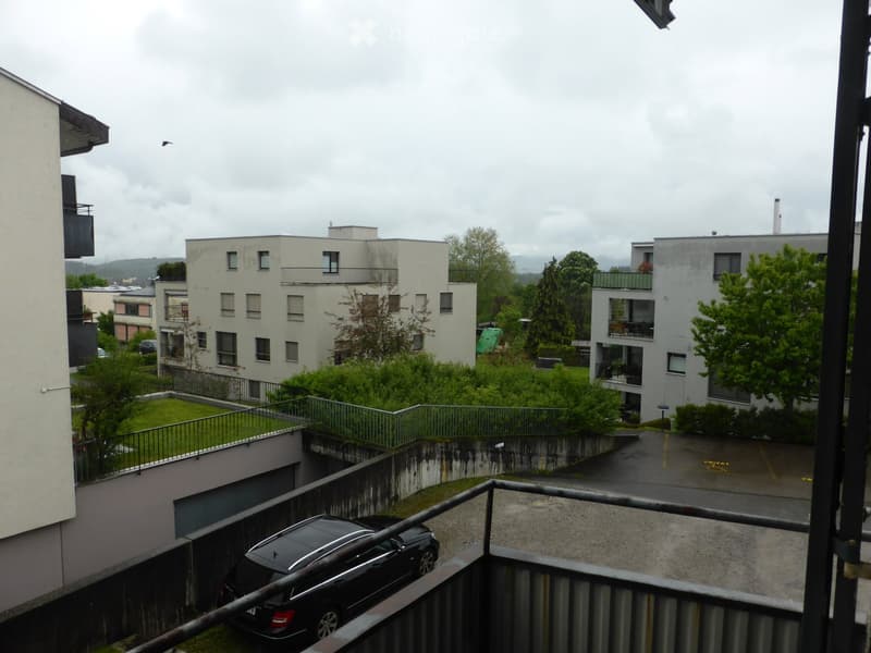 Balcony overlooking a residential area with multiple apartment buildings, greenery, and a parking area below.