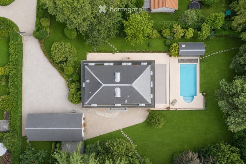 Aerial view of a well-maintained garden with a swimming pool, a modern house, and surrounding greenery.