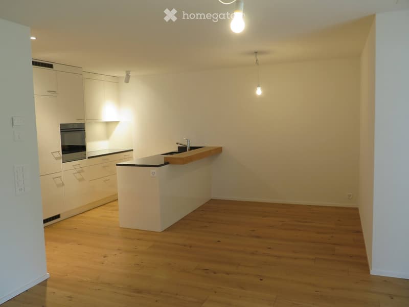 Empty kitchen with white cabinets, wooden countertop, and wooden flooring.