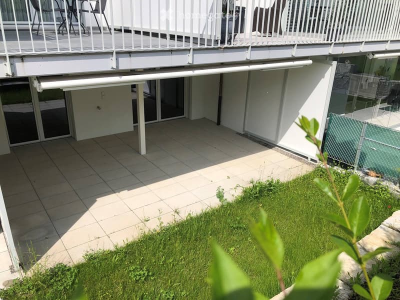 Balcony area with tiled floor, white railing, and small garden patch with grass and plants.