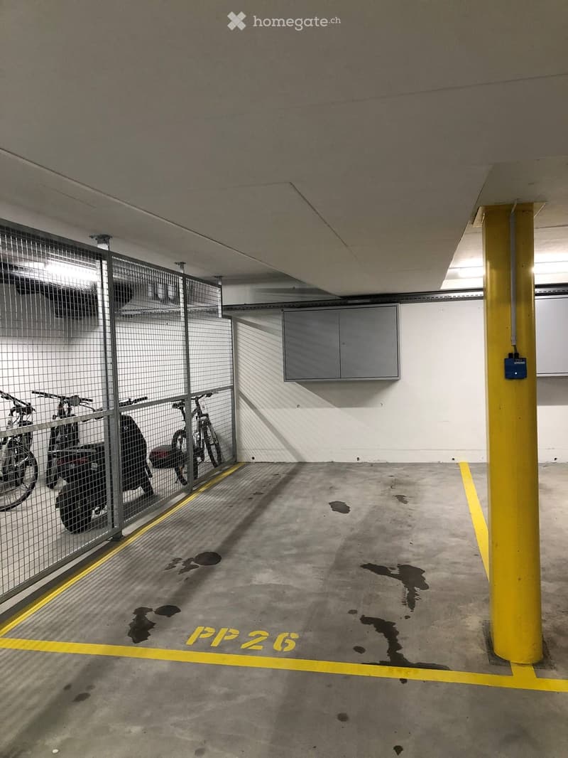 Underground parking area with concrete floor, yellow painted lines, and a fenced section containing bicycles and a motorcycle.