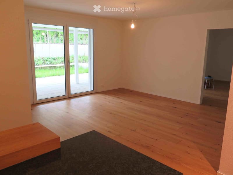 Empty room with wooden flooring, large sliding glass doors leading to a patio, and a small bench near the entrance.