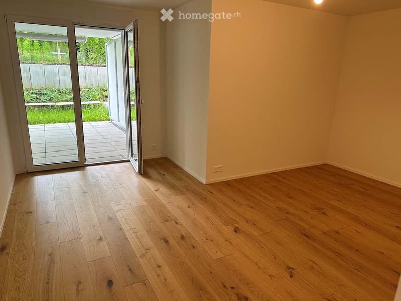Empty room with light wooden flooring and large sliding glass doors leading to a patio and garden area.