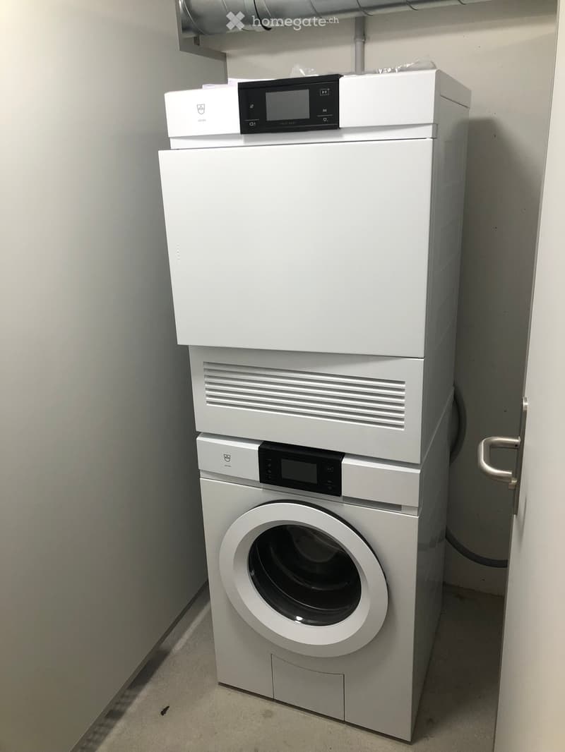 A compact bathroom with a stacked washing machine and dryer unit, featuring a control panel on top of the dryer.