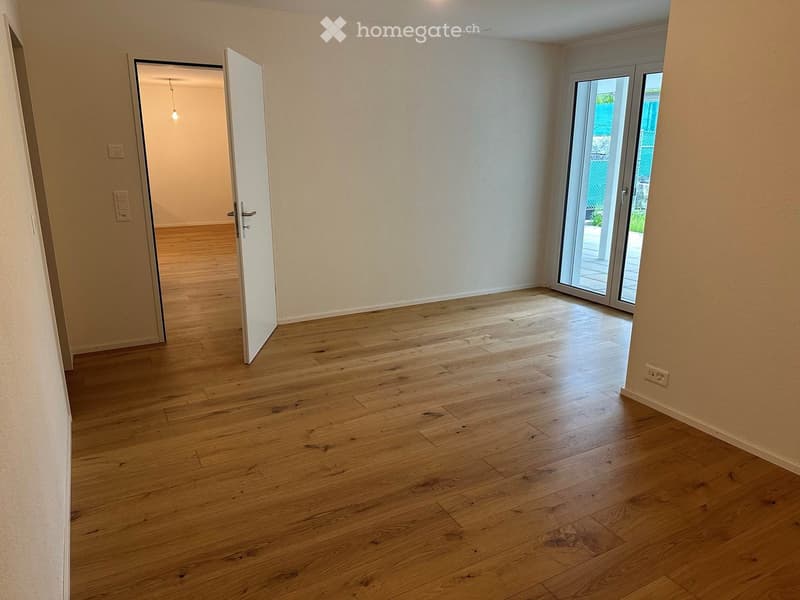 Empty room with wooden flooring, white walls, and a sliding glass door leading to an outdoor area.